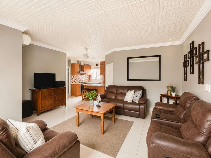 Open-plan living area featuring tiled floors, a textured ceiling, and a functional kitchen with wooden cabinetry and integrated appliances.
