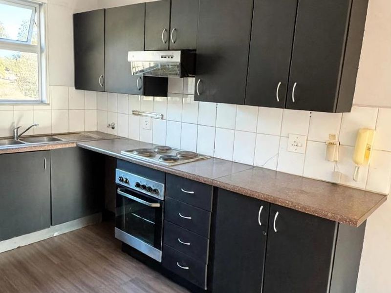 A functional kitchen featuring dark cabinetry, laminate countertops, built-in oven, hob, and extractor fan, with a tiled backsplash and laminate flooring.