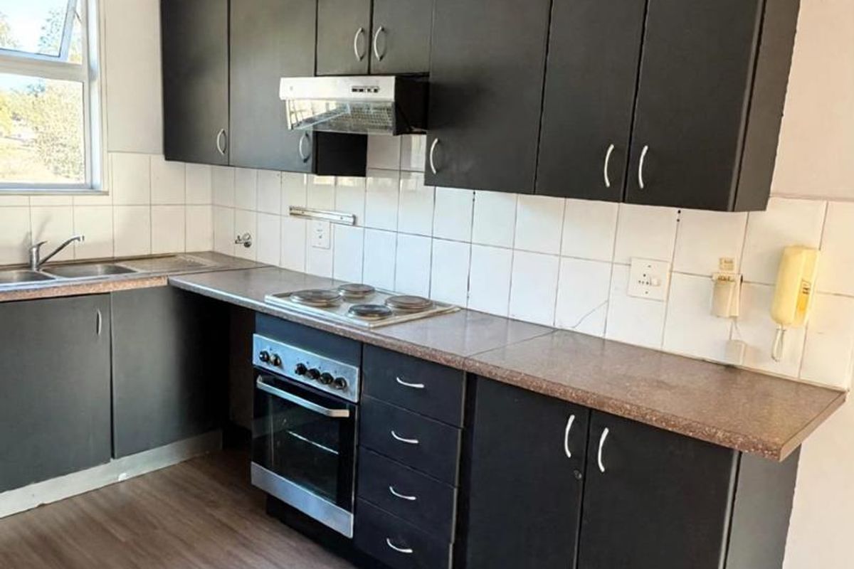 A functional kitchen featuring dark cabinetry, laminate countertops, built-in oven, hob, and extractor fan, with a tiled backsplash and laminate flooring.
