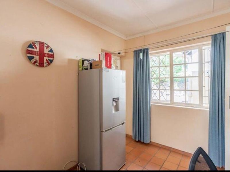 A compact kitchen area featuring terracotta floor tiles, a window with security bars, and coved ceilings, requiring cosmetic updates to improve its overall condition.