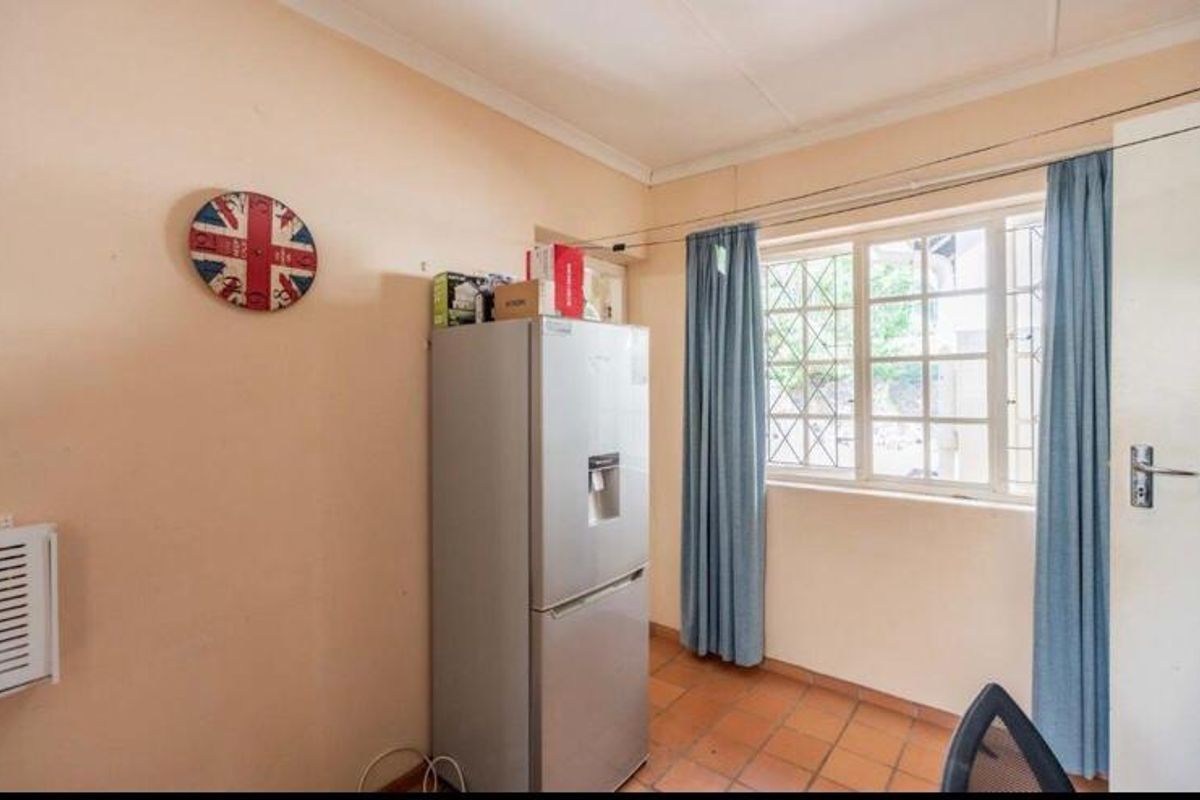 A compact kitchen area featuring terracotta floor tiles, a window with security bars, and coved ceilings, requiring cosmetic updates to improve its overall condition.