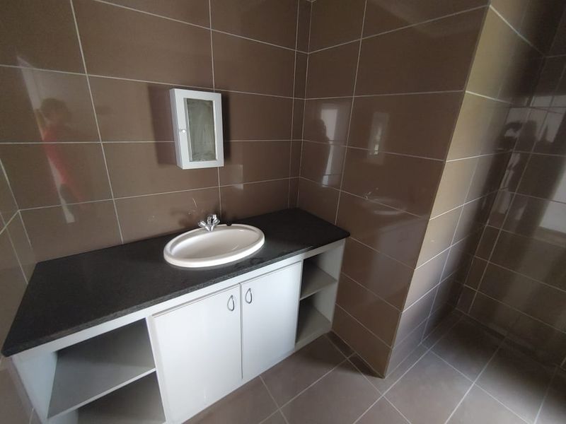A clean bathroom featuring a vanity cabinet with a granite countertop, drop-in basin, and full-height ceramic wall tiling.