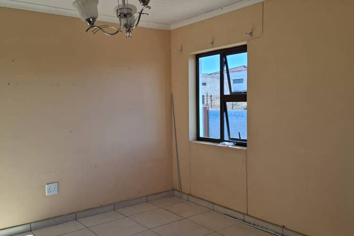 An empty living room featuring tiled flooring, a central chandelier, and a window with security bars.