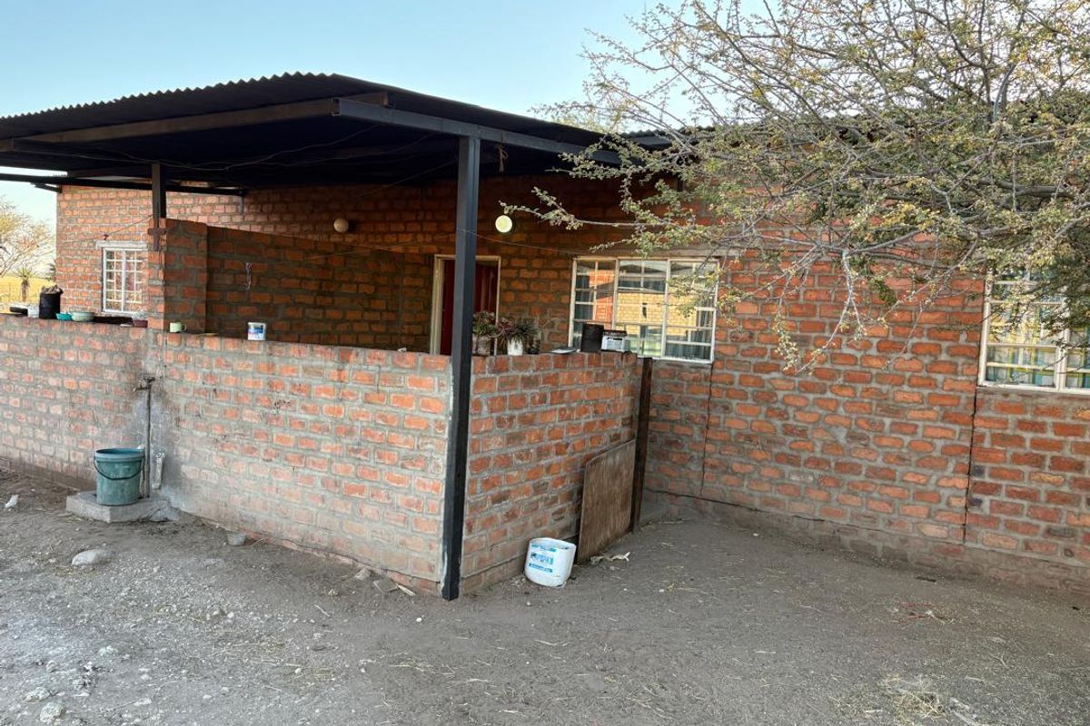 A rustic farm-style exterior featuring an exposed brick facade with a covered patio area and simple metal roofing.