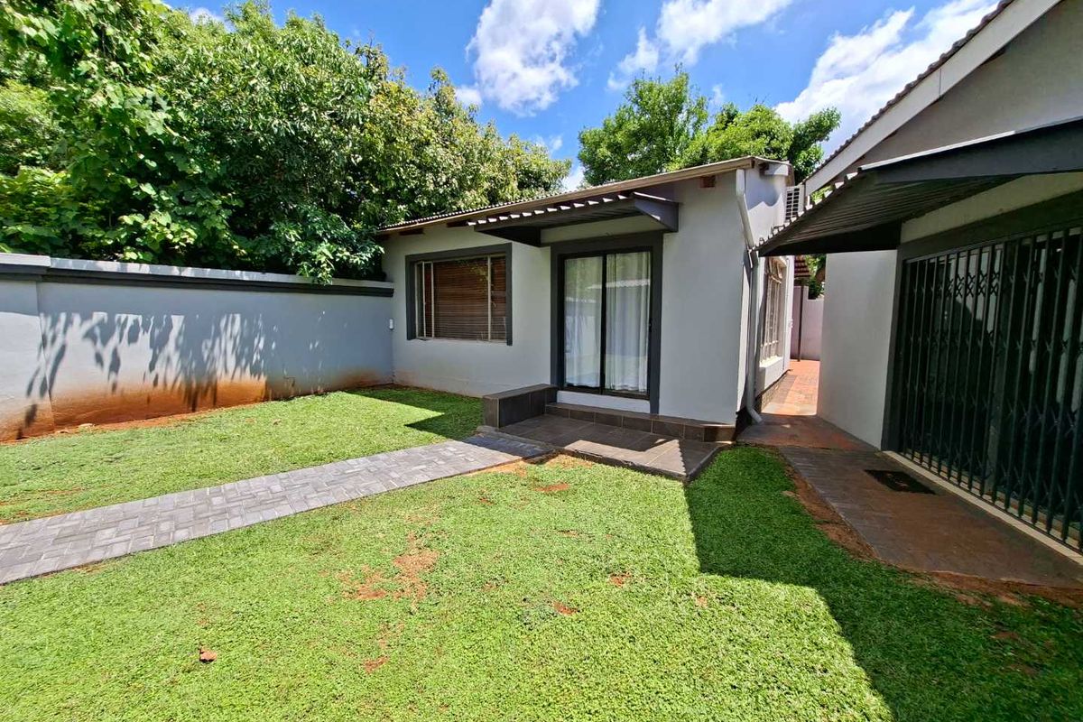 A well-maintained rear exterior view featuring a paved walkway, manicured lawn, and a covered patio area with sliding glass doors.