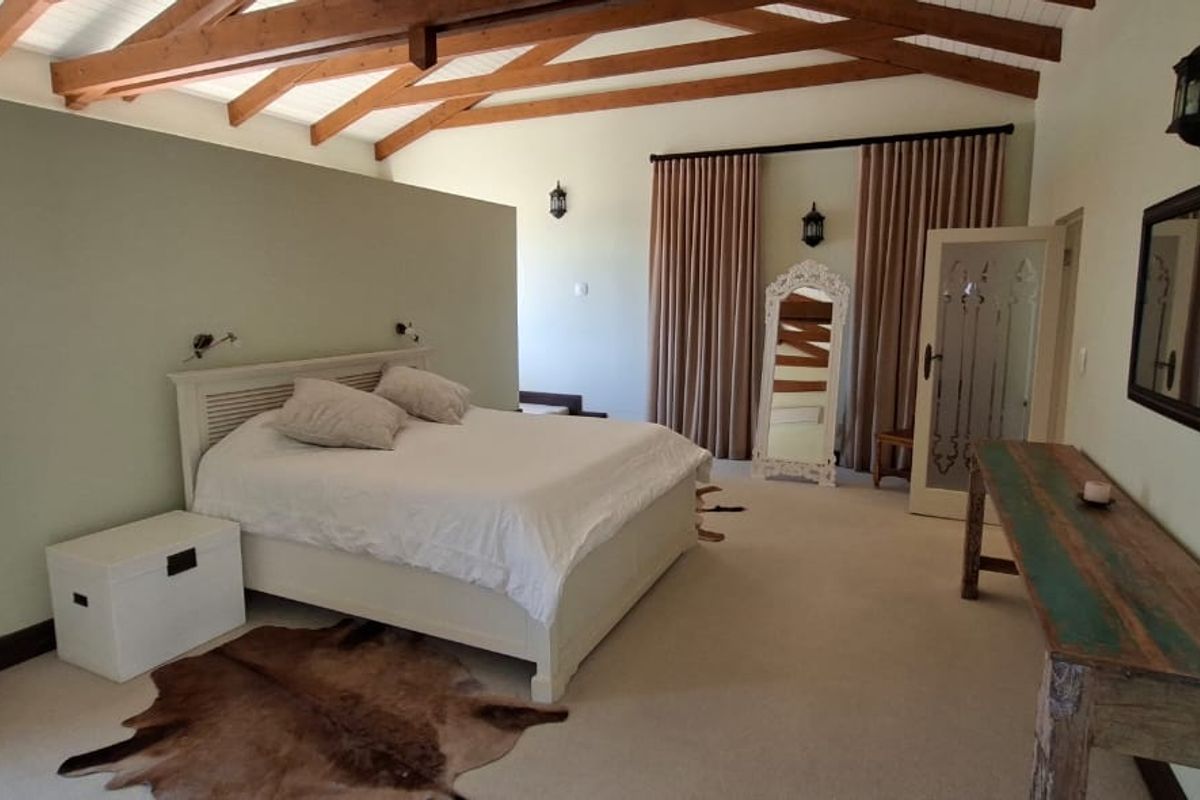 Spacious bedroom featuring a vaulted ceiling with exposed timber beams, neutral carpeting, and wall-mounted lighting, creating a warm and inviting atmosphere.