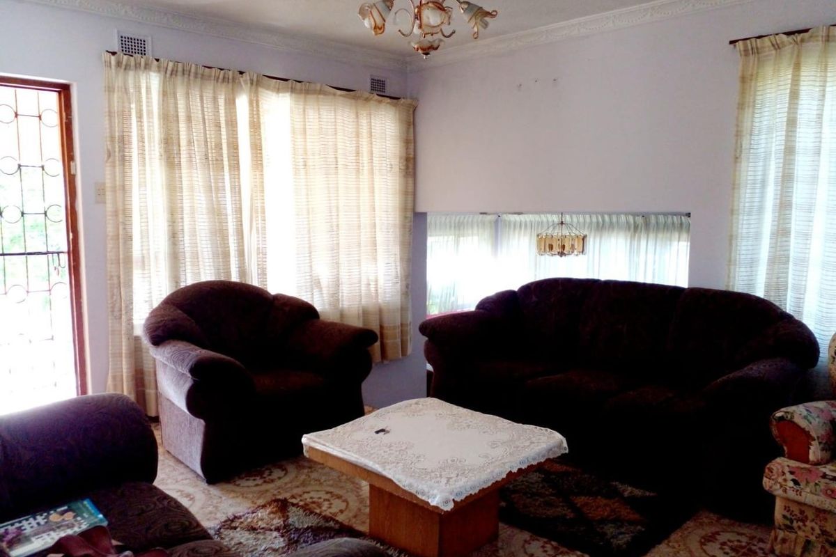 A traditional living room featuring decorative ceiling cornices, a central light fixture, and large windows with security access to the exterior.