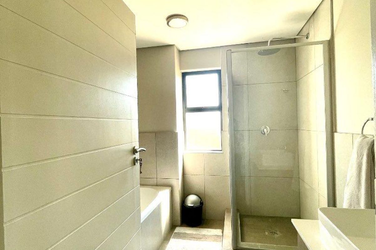 Modern bathroom featuring a glass-enclosed shower, a built-in bathtub, and a sleek vanity with a vessel sink, finished with neutral floor-to-ceiling tiling.