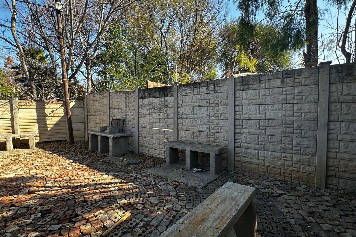 Outdoor entertainment area featuring a concrete boundary wall, built-in concrete benches, and a brick-paved courtyard space.