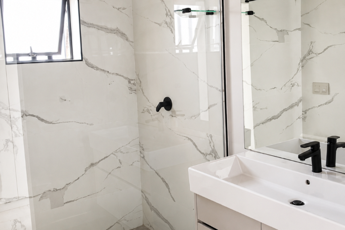 Modern bathroom featuring a walk-in shower with marble-look tiling, black matte fixtures, and a sleek vanity cabinet with a large mirror.