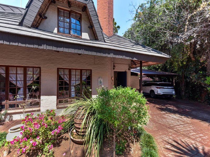 Front elevation of a charming cottage-style house featuring a thatched roof, brick chimney, timber-framed windows, and a paved driveway with a carport.