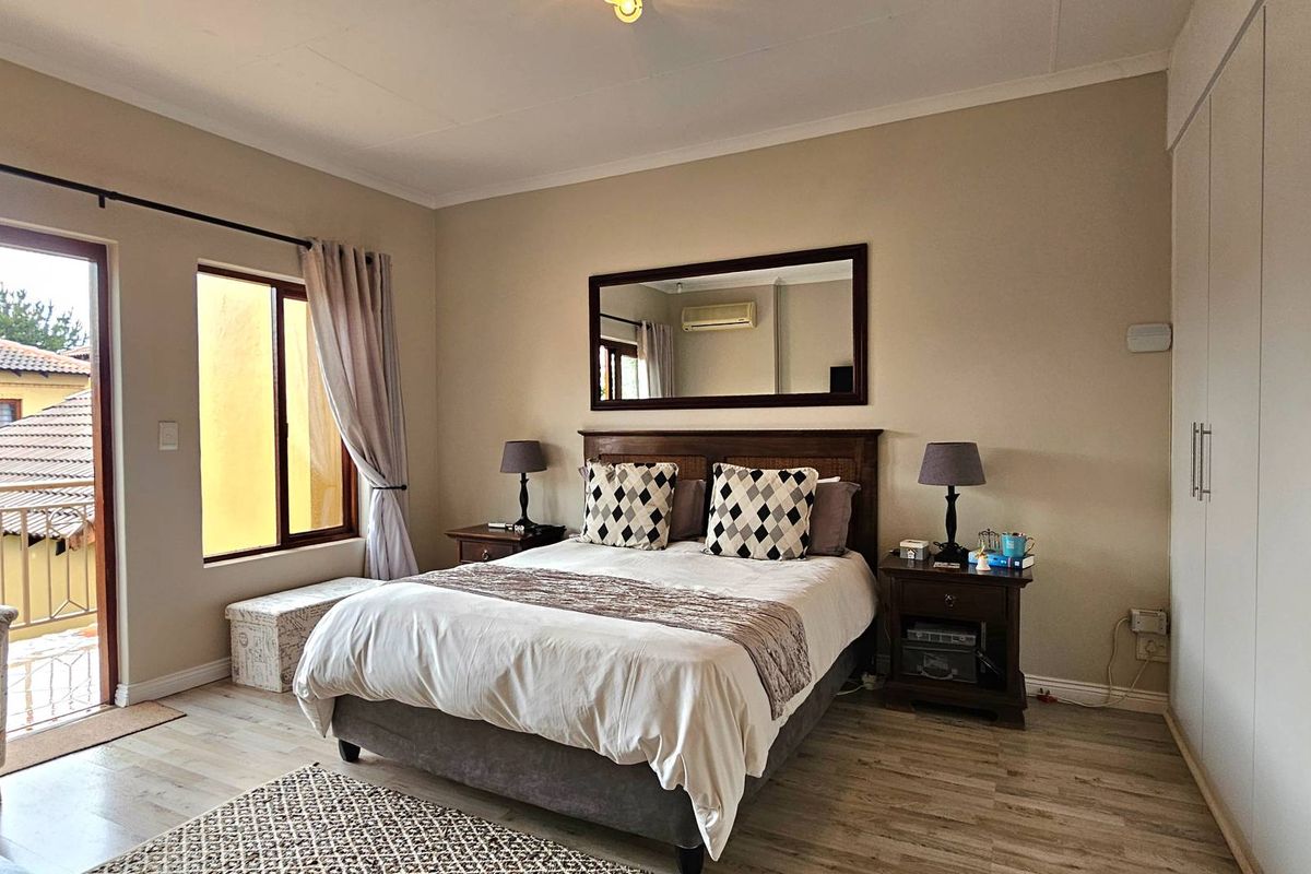 A well-maintained bedroom featuring light wood-look flooring, built-in floor-to-ceiling wardrobes, and direct access to a private balcony through a glass door.