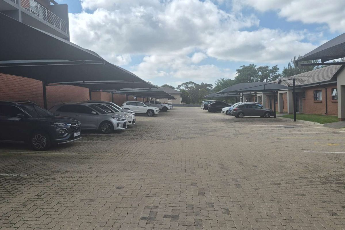 A paved outdoor parking area featuring covered carports for residents, situated within an apartment complex setting.