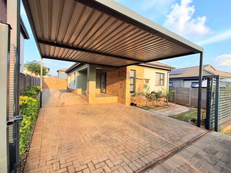 Front exterior view featuring a paved driveway, a modern metal carport, brick facade detailing, and a secure sliding gate entrance.