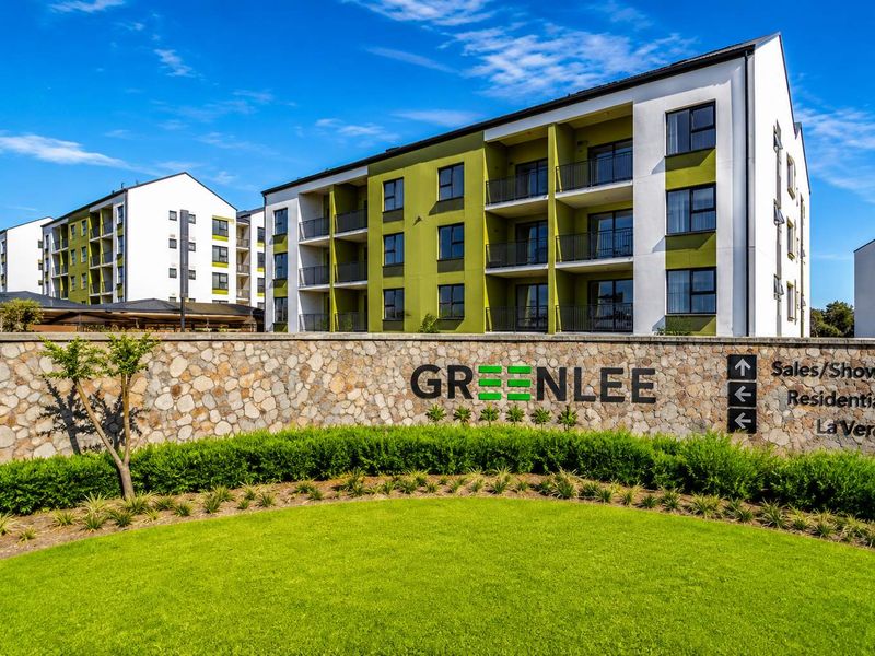 Exterior view of the Greenlee residential estate featuring a stone-clad entrance wall, manicured lawn, and modern multi-story apartment buildings with balconies.