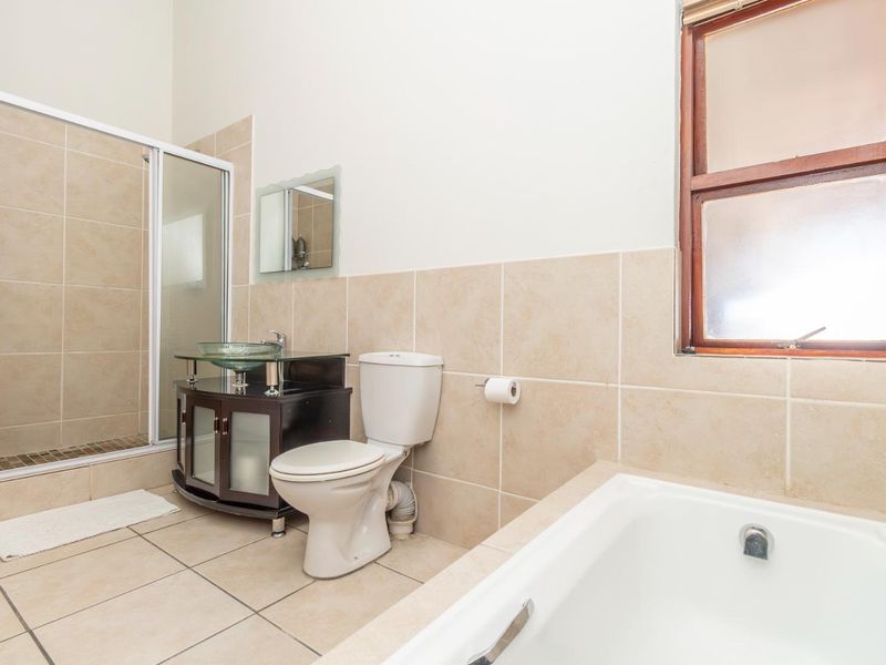 A functional bathroom featuring a glass vessel sink, vanity cabinet, separate shower enclosure, and a bathtub with neutral wall and floor tiling.