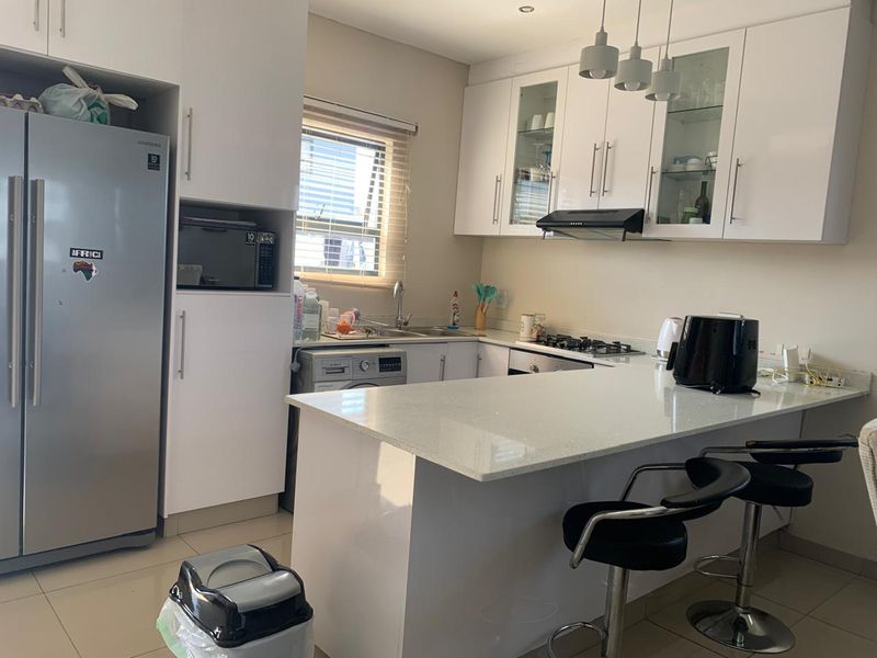 Modern kitchen featuring white cabinetry, quartz countertops, a gas hob, extractor fan, and integrated space for appliances, including a breakfast bar area.