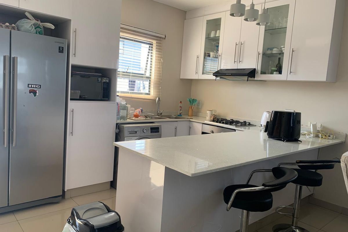 Modern kitchen featuring white cabinetry, quartz countertops, a gas hob, extractor fan, and integrated space for appliances, including a breakfast bar area.