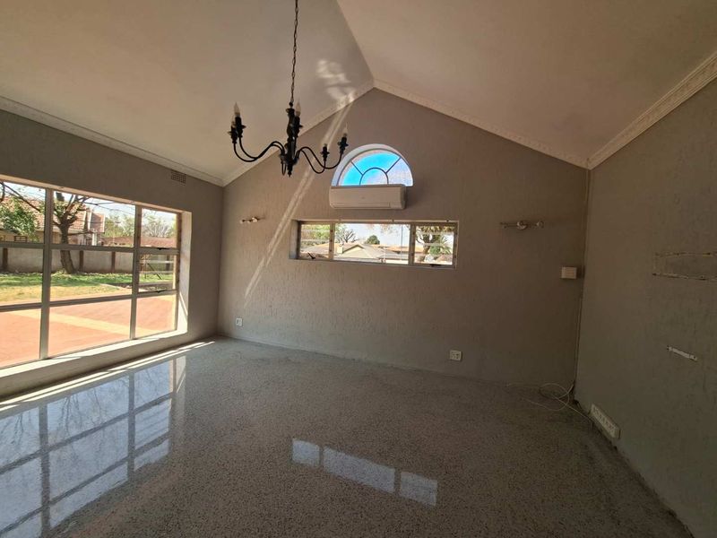Spacious living room featuring a vaulted ceiling, polished terrazzo flooring, an arched window, and a split-system air conditioner.