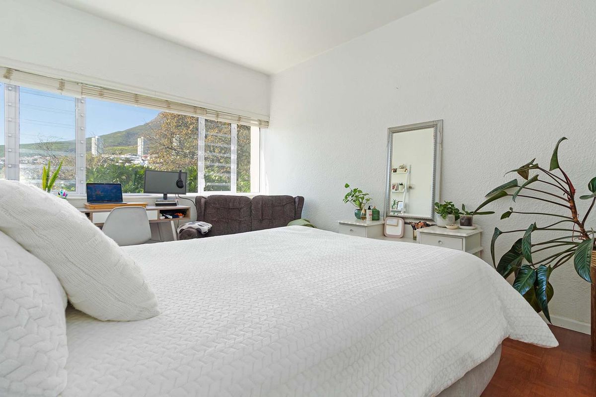 A bright bedroom featuring parquet flooring and a large window offering natural light and scenic views.