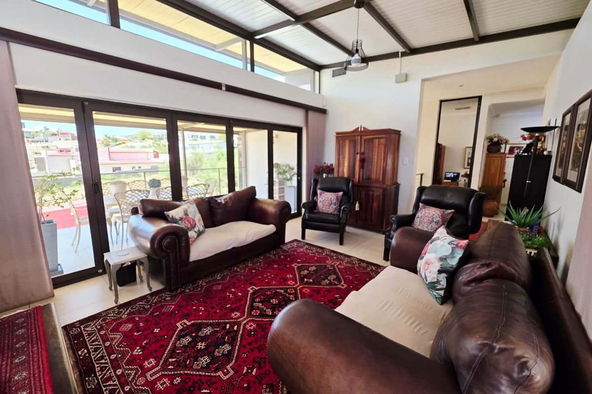 Spacious living room featuring high exposed beam ceilings, clerestory windows for natural light, and large sliding glass doors opening to an outdoor patio area.