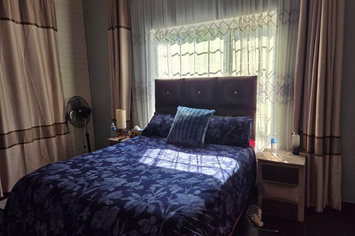 A cozy bedroom featuring tiled flooring and a window with security bars, dressed with curtains.