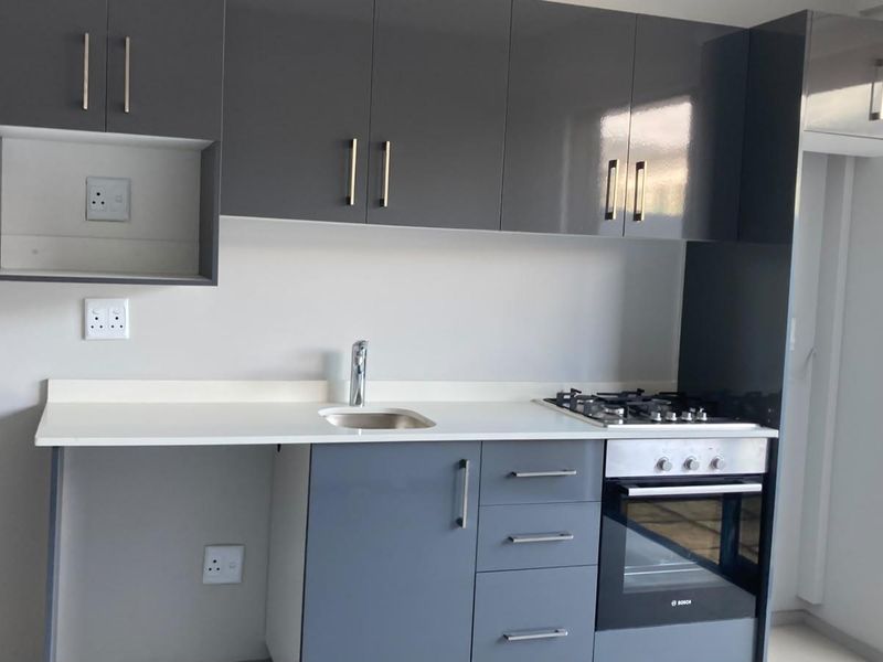 Modern kitchen featuring sleek grey cabinetry, white countertops, integrated gas hob, and built-in oven in a clean, contemporary apartment setting.