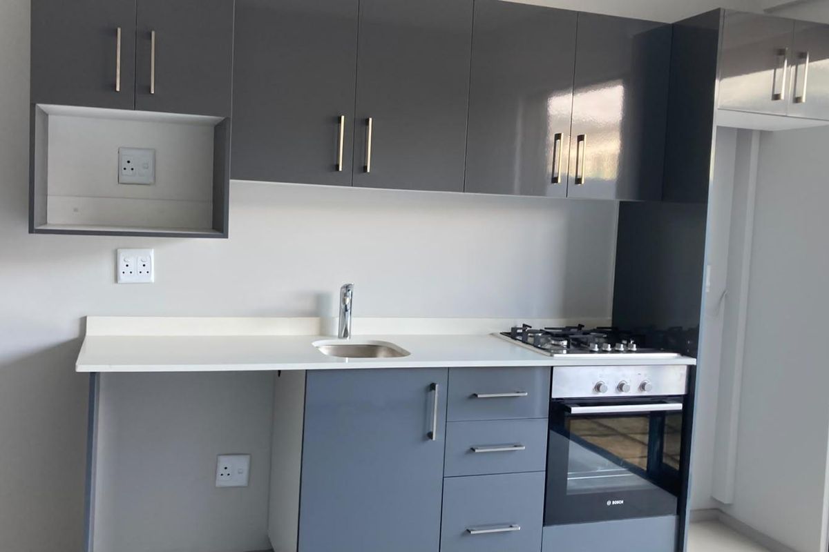 Modern kitchen featuring sleek grey cabinetry, white countertops, integrated gas hob, and built-in oven in a clean, contemporary apartment setting.
