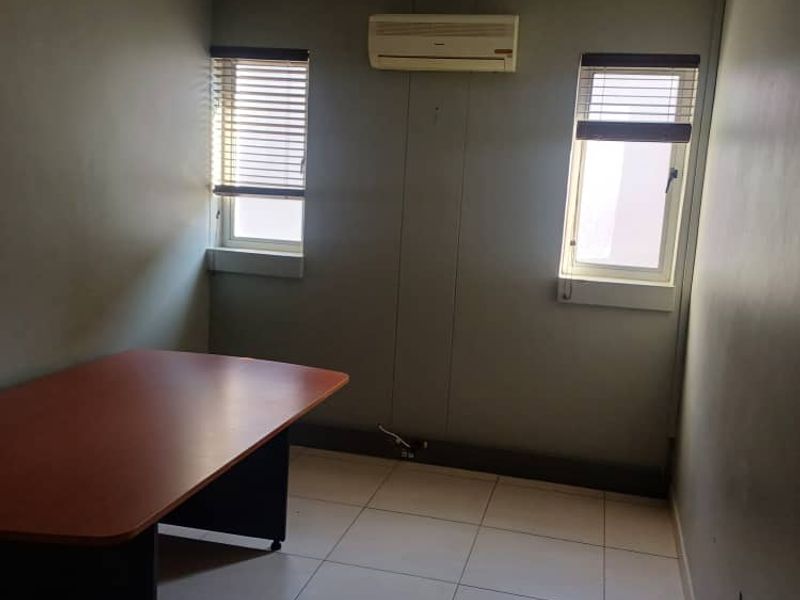 A functional office space featuring tiled flooring, a suspended ceiling with integrated lighting, and a wall-mounted air conditioning unit.