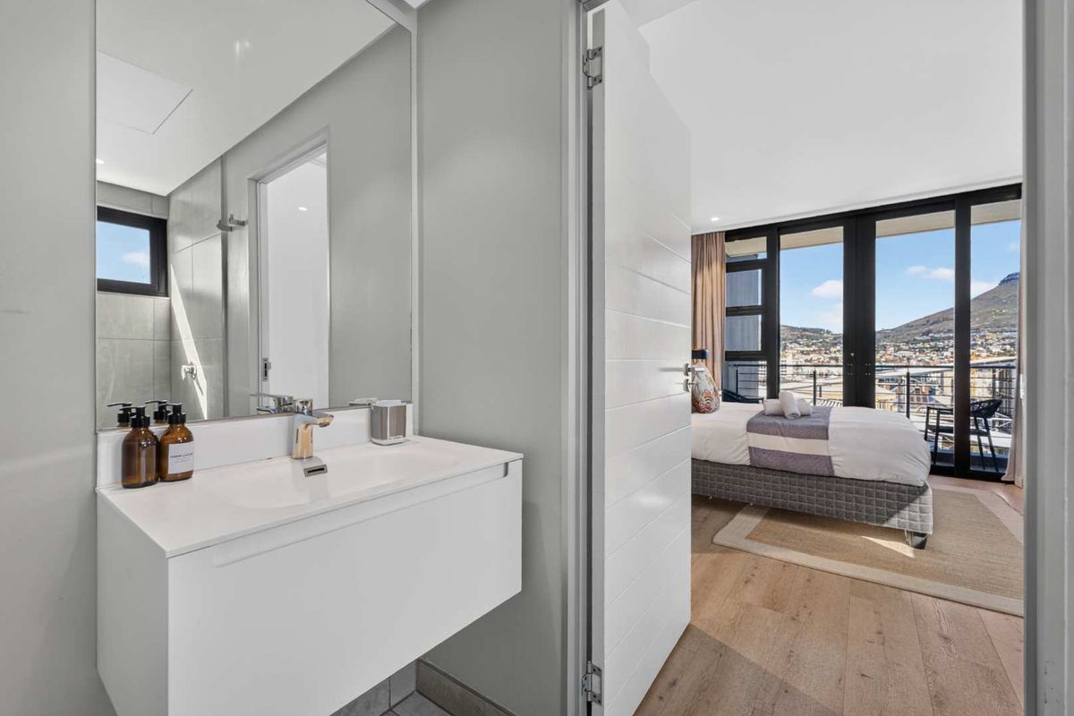 Modern bathroom featuring a sleek wall-mounted vanity with basin and large mirror, with a view through to the adjacent bedroom and balcony.