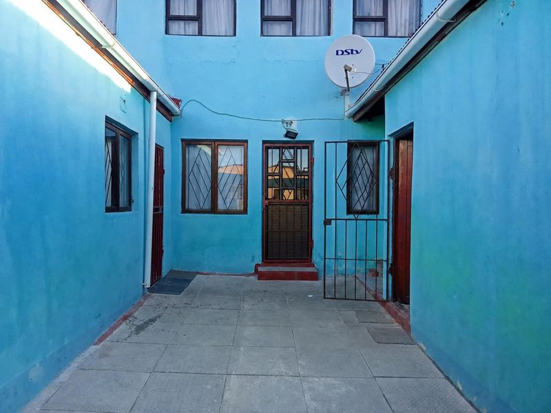A paved rear courtyard area featuring security gates and access points to the main dwelling, with visible wear to the exterior wall finishes.