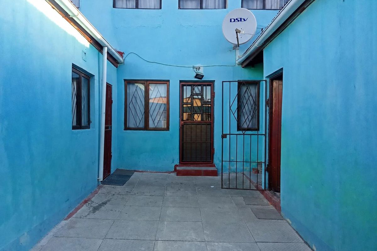 A paved rear courtyard area featuring security gates and access points to the main dwelling, with visible wear to the exterior wall finishes.