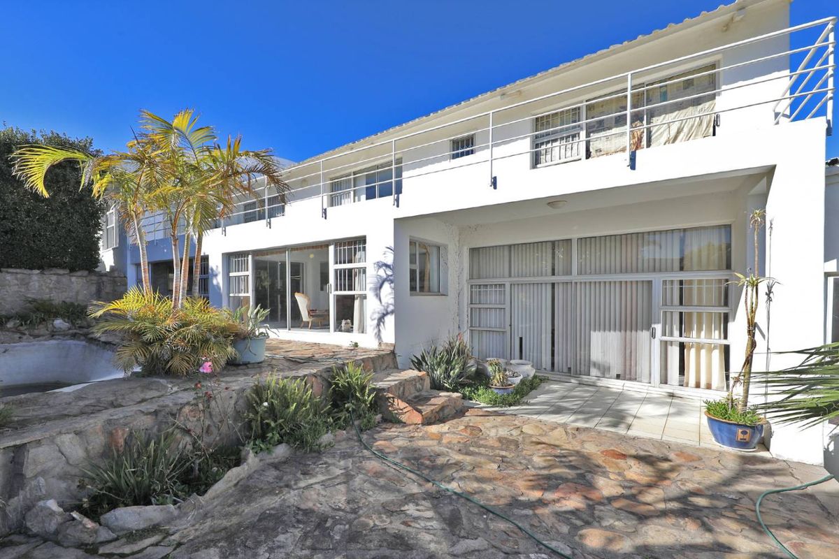 Rear view of a multi-level home featuring a stone-paved patio, swimming pool, and upper-level balcony with metal railings.