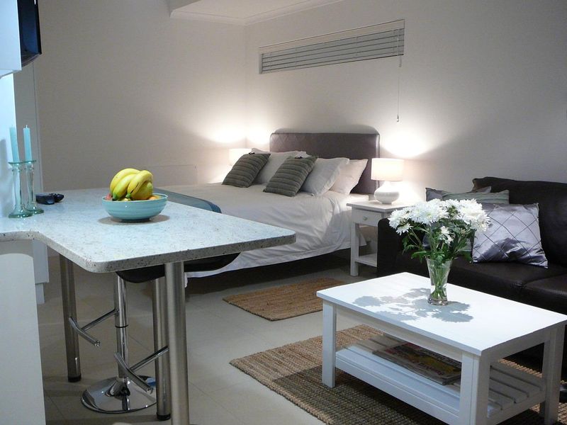 An open-plan studio space featuring a stone breakfast bar, neutral tiled flooring, and integrated lighting, creating a functional living and sleeping area.