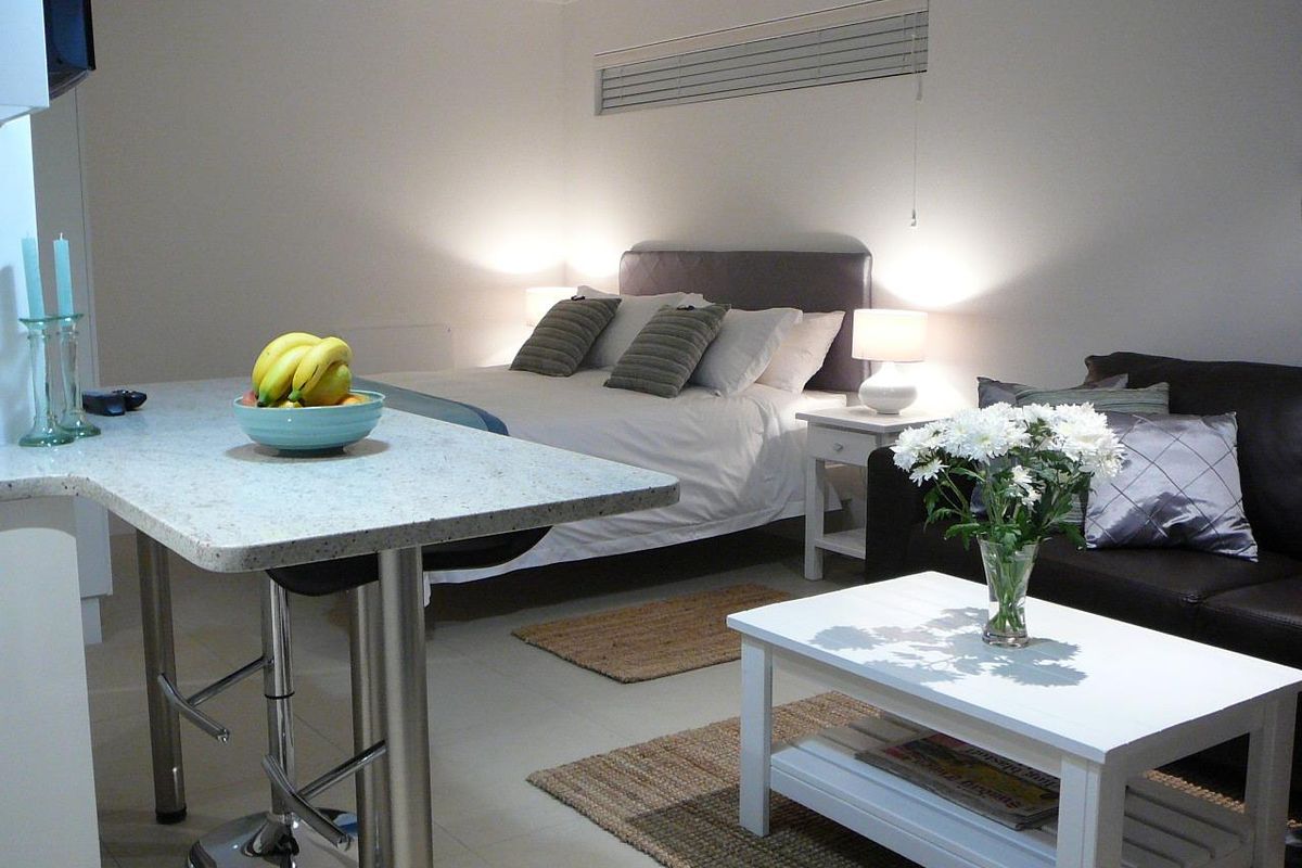 An open-plan studio space featuring a stone breakfast bar, neutral tiled flooring, and integrated lighting, creating a functional living and sleeping area.