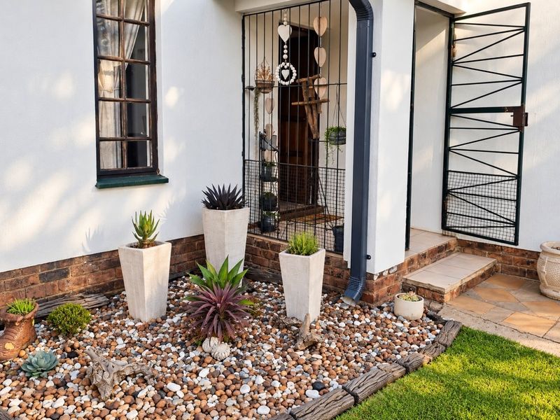Front entrance area featuring a security gate, tiled step, and a landscaped garden bed with decorative stone and established plants.
