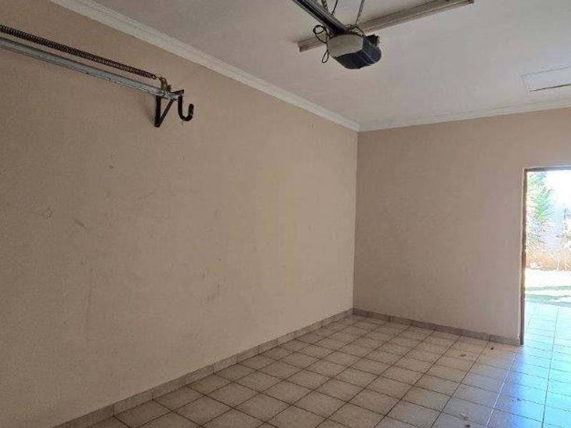 A vacant garage space featuring tiled flooring, a ceiling access hatch, and an installed garage door motor with tracks.
