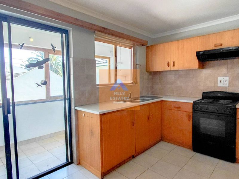 A functional kitchen featuring laminate cabinetry, tiled backsplash, and a freestanding stove, with direct access to an adjacent balcony through a sliding glass door.