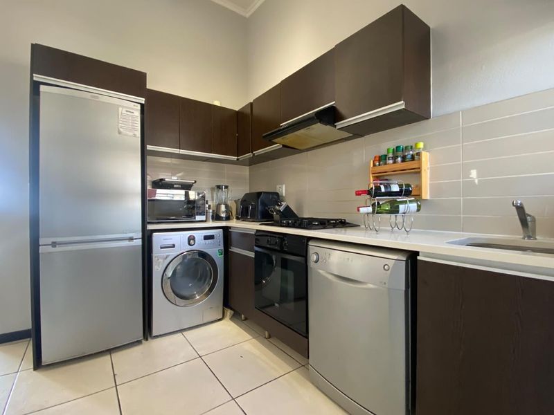 A functional kitchen featuring dark wood cabinetry, white stone countertops, a built-in oven, gas hob, and tiled backsplash with integrated appliance spaces.