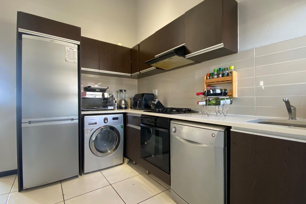 A functional kitchen featuring dark wood cabinetry, white stone countertops, a built-in oven, gas hob, and tiled backsplash with integrated appliance spaces.