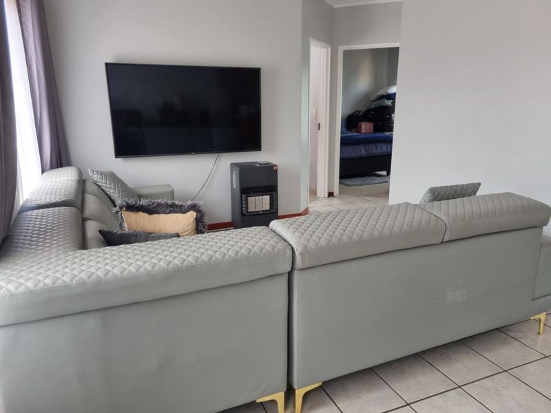 A living room area featuring tiled flooring and a wall-mounted television, with a view leading into an adjacent bedroom.