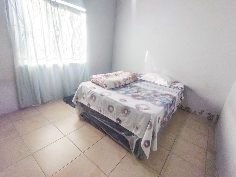 A bedroom featuring tiled flooring and a window, showing visible signs of wall dampness and paint deterioration requiring maintenance.