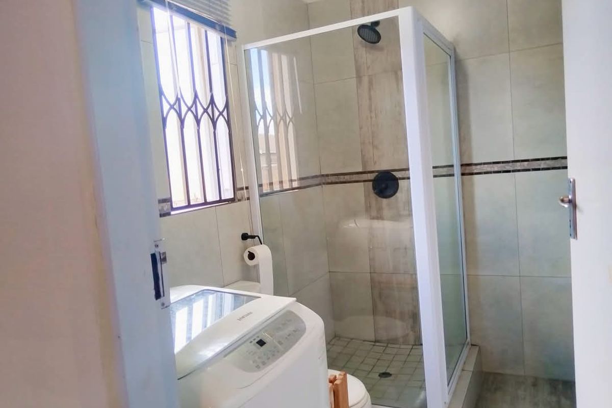 A functional bathroom featuring a glass-enclosed shower, tiled walls, and a window with security bars.