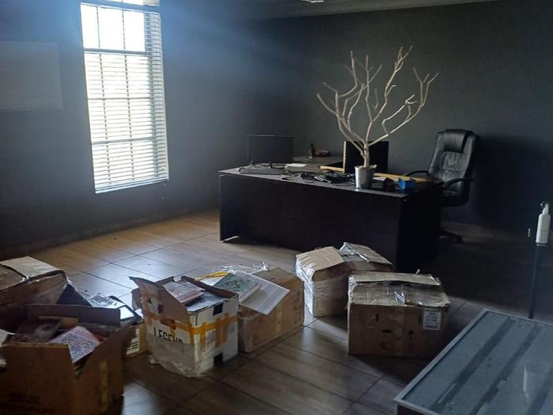 A dimly lit office space featuring tiled flooring, recessed lighting, and a window with venetian blinds, currently showing signs of ceiling wear.
