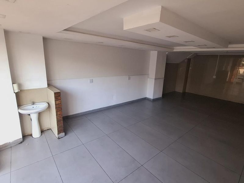 An open-plan commercial or utility space featuring large format floor tiles, a pedestal washbasin, and a modern bulkhead ceiling with recessed lighting.
