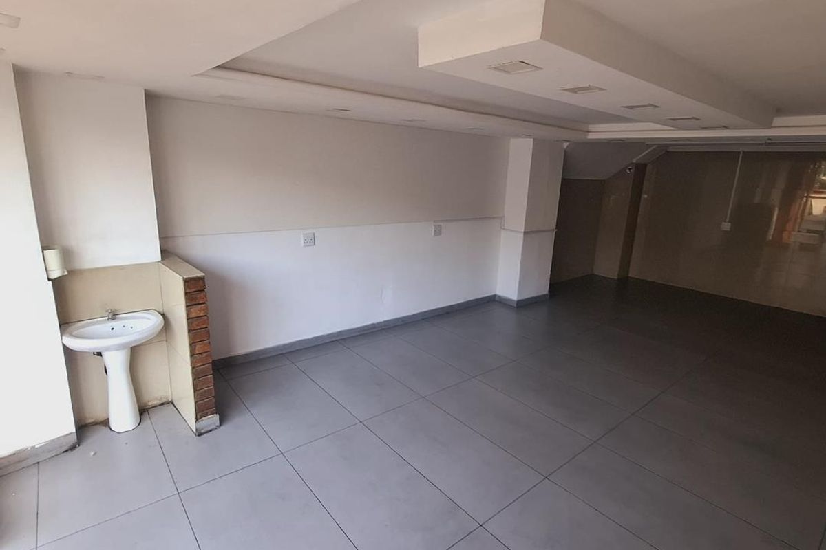 An open-plan commercial or utility space featuring large format floor tiles, a pedestal washbasin, and a modern bulkhead ceiling with recessed lighting.