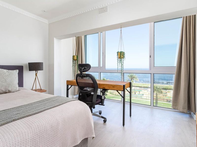 A bright, modern bedroom featuring large sliding windows with expansive ocean views, crown molding, and neutral laminate flooring.