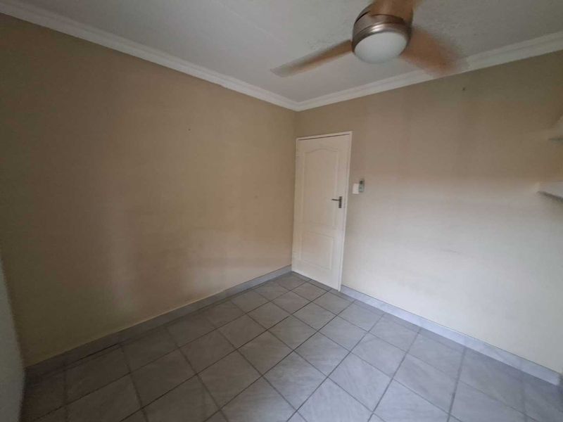 An empty bedroom featuring tiled flooring, a ceiling fan, and neutral wall finishes, offering a blank canvas for personalization.