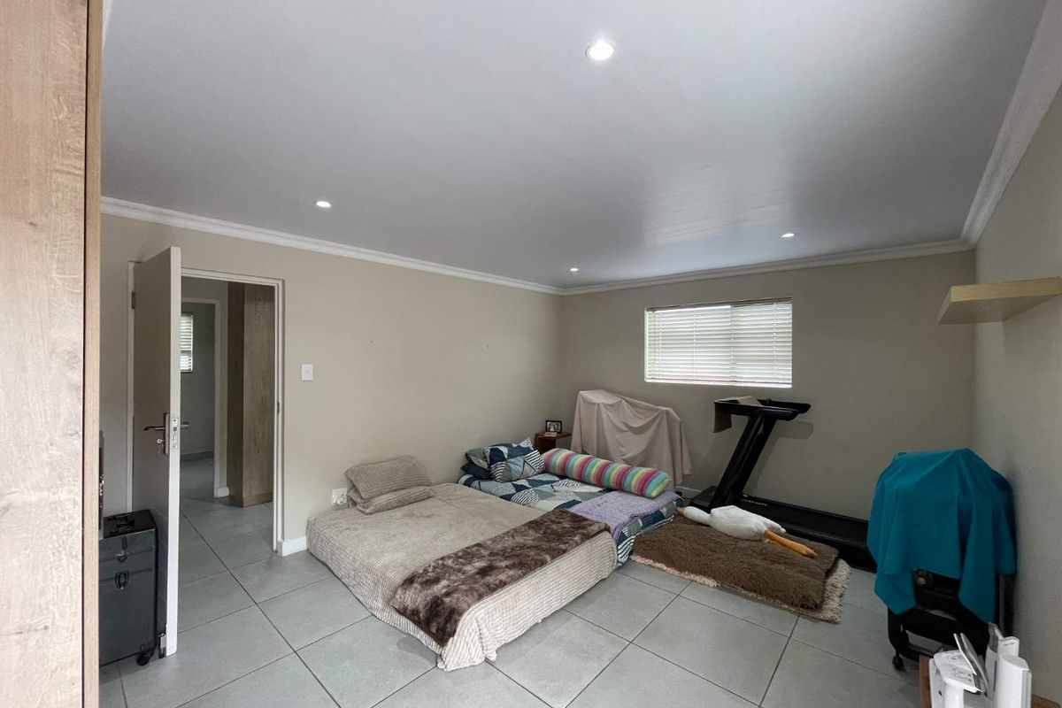 A spacious bedroom featuring neutral wall tones, large format floor tiles, recessed ceiling lighting, and a window fitted with horizontal blinds.