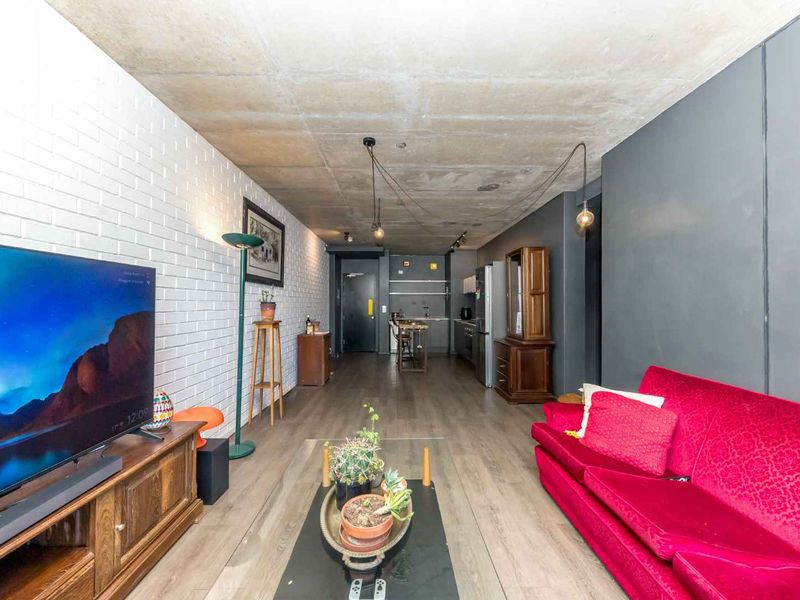 Open-plan living area featuring an exposed concrete ceiling, white brick feature wall, and a modern kitchen layout with integrated cabinetry.